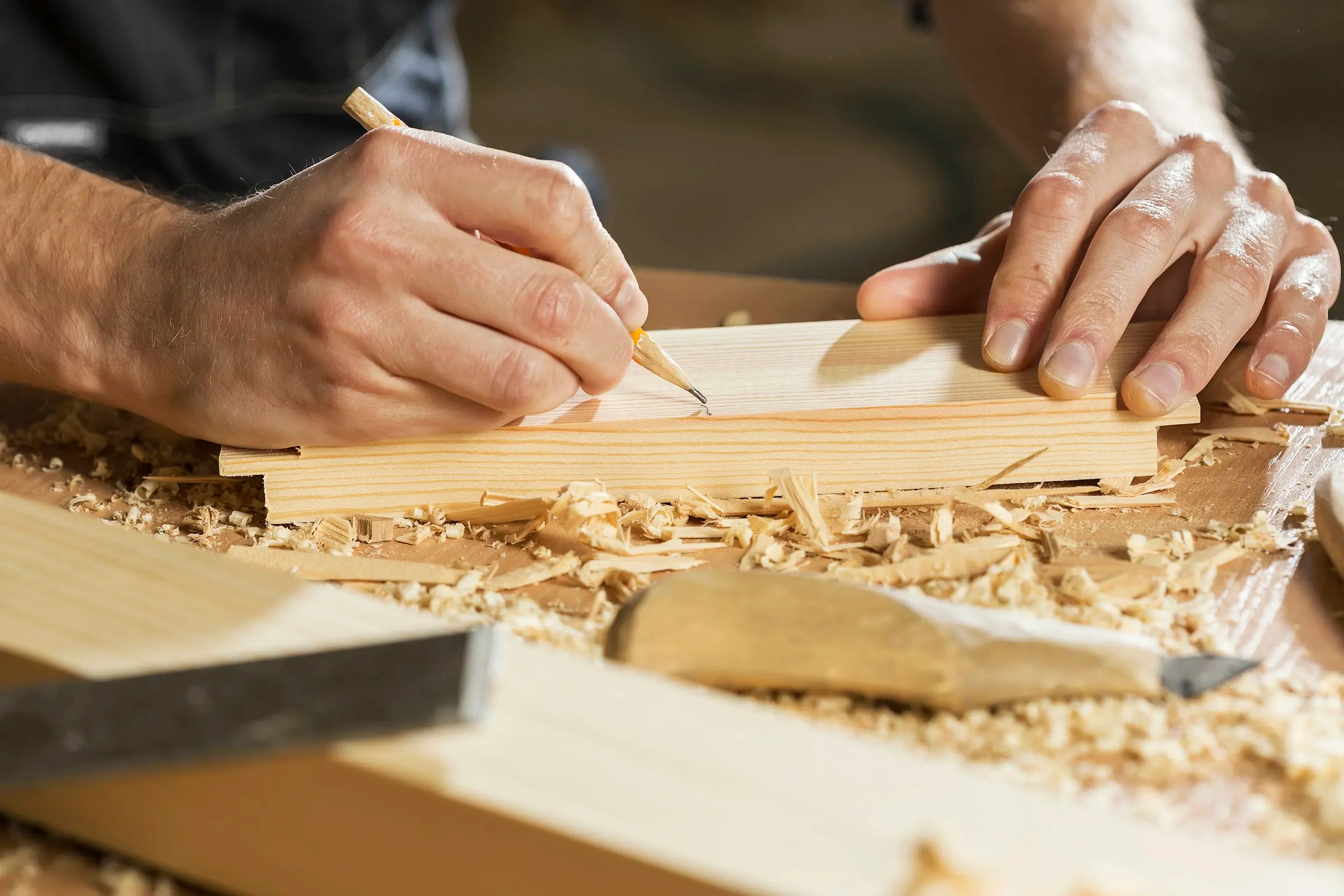 Hände reißen mit einem Bleistift eine Linie auf einem Holzbrett an